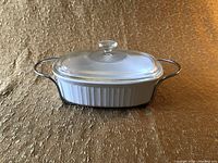 Side view of vintage Pyrex casserole with clear glass lid in place shown on textured gold fabric background.