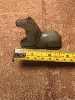 Photo of small carved jade horse figurine lying on textured fabric with measuring tape showing length about 2 inches