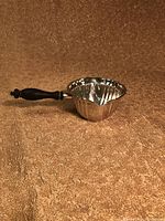 Side view of sterling silver long handled sauce boat showing fluted design and wooden handle.