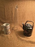 Full view of three items: ceramic pitcher, tall glass tower, black Asian style teapot