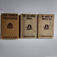 Front covers of three vintage Hardy Boys books titled 'The Tower Treasure,' 'The Clue in the Embers,' and 'The Secret of Pirates' Hill' showing cloth binding and printed titles.