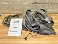Electric heated shawl with visible USB connector and user manual shown beside it.