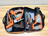Open soft-sided orange carrying case showing multiple plastic toy tools in orange, gray and black colors including hammer, jigsaw, wrench, handsaw, flashlight, screwdriver, and drill