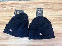 Front side of two black Dickies beanies with logo patches on cuffs, tags attached.