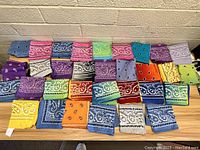 31 bandanas in various colors and patterns neatly folded and displayed on a floor.