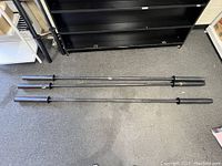 Full-length view of three black squat bars placed on carpeted floor showing overall condition and length differences.