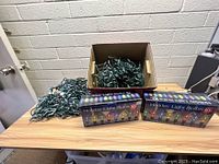 Box and loose strands of green wired Christmas holiday lights on a wood table.
