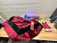 Full view of Christmas tree skirt, string lights, Ho Ho Ho button covers, and angel tree topper on a table