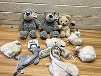 Full lot showing all plush items on table: two gray bears, one cream bear, three white geese, small whale, snuggle plush.