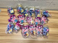 Photo showing all plush toys laid out on a wooden surface, with multiple copies of Super Grover and Abby Cadabby characters in sealed plastic packaging.