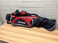 Full view of the Nitro branded black and red golf bag resting on a wooden table.
