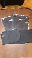 3 black fitted active shirts in original packaging and 3 black loose t-shirts laid out on table