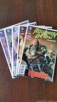 Five Aquaman and Others comic books fanned out on a wooden surface, showing covers including issue #1 with title 'Payback!'