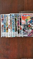 Photo shows a row of 10 Justice League comic books laid out on a wooden surface. The comics have colorful and detailed covers with the DC Comics logo visible. The comics appear in excellent condition and mostly in sequence.
