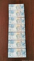 Front and back views of seven Canadian $5 polymer banknotes stacked and spread out showing the sequential serial numbers and design details.