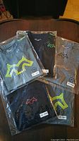 Four packaged new fitted active shirts displayed flat with different logo prints.