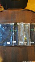 Photo showing two fitted active workout shirts in original sealed packaging, flat on table.