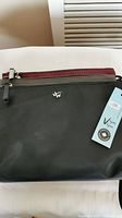 Front view of handbag showing black compartment with silver logo and the tops of grey and burgundy compartments under zippers.