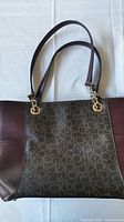 Front side of Calvin Klein mahogany handbag showing CK monogram pattern and leather sides with gold-tone ring attachments