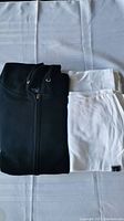 Folded black zipper hoodie next to two folded white t-shirts on a white surface.