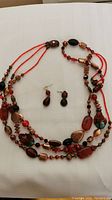 Photo of the multi-strand necklace made of red and brown beads with two red tone bead drop earrings