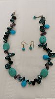 Photo of a turquoise and dark green stone bead necklace with teardrop accents along with matching small turquoise bead dangle earrings.
