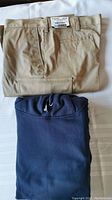 Folded khaki cargo pants with visible tag and folded navy blue pullover hoodie on white fabric background.