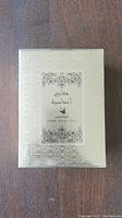 Front of gold patterned box with Arabic script and floral design framing perfume details including 100ml volume.
