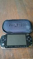 Front view of Sony PSP console with screen and controls visible beside the black protective case with embossed PSP on front.