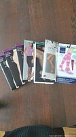 7 packages of pantyhose and long socks on wooden surface, new in original packaging. Brands include Express, Smart & Sexy, Jockey, and Sigvaris.
