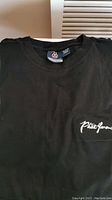 Close-up of black t-shirt tag and small white logo on chest pocket area