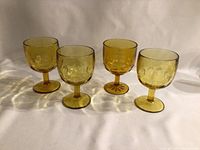 Four large amber goblets with round bases and short stems, arranged in a row on white background.