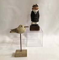 Full view of the carved captain on a wooden block stand and seagull on a separate wooden base with metal rod