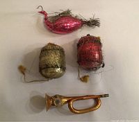 Photo showing all four antique glass Christmas ornaments on a flat surface: red bird, two acorns wrapped in metal netting, and gold-tone bugle.