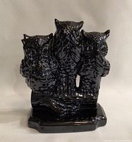 Front view of three black ceramic owls with metallic sheen on a branch base, showing detailed texture and the unique 'hear no evil' pose.