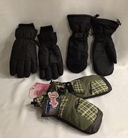 Photo of two pairs of black men’s winter gloves and mitts alongside one pair of green plaid women’s mitts