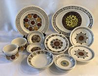 Group photo of all brown and yellow ceramic dishware pieces showing plates, bowls, and mugs with floral patterns in brown, yellow, and cream.