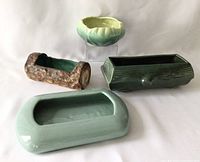 Four ceramic planters including large light green rectangular planter, dark green wood textured planter, brown log shaped planter, and pale green scalloped bowl