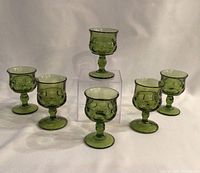 Front view of six green glass King's Crown Thumbprint glasses arranged with one elevated in the back.