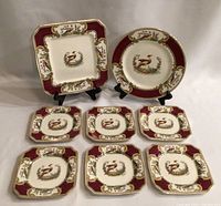 Full set of eight dishes displayed with two on stands: one large square and one round plate behind seven smaller square plates, showing design and condition.
