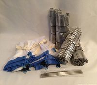 Photo showing multiple bundles of stainless steel straw sets and several reusable produce bags in blue and white, laid out on surface.