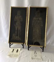 Pair of framed vintage brass rubbings depicting Henry Paris and John Trembral, displayed with explanatory papers and stands. Frames show general light wear; one glass pane has minor scratch visible.