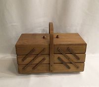 Closed view of the large wooden sewing basket with a central handle and visible diagonal wooden pullout mechanism.