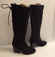 Side view of tall black boots with back lacing and side zipper, showing the mid-height heel and toe shape.