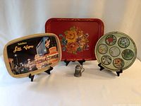 Full view of lot showing three decorative tin trays on stands and one miniature beer stein figurine in front