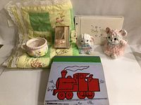 Overall photo showing all items: 3 ceramic baby planters, green and yellow baby quilt, comb and brush set in box, baby photo album, and 6 wooden puzzle boards.