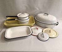 Vintage enamelware assortment including baking dishes, saucepans with handles, and a roasting pan with lid arranged together showing overall lot contents.