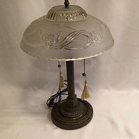 Full view of vintage table lamp showing heavy frosted glass shade with floral pattern, metal base, pull chains with tassels, and power cord.