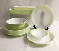 Photo showing full assortment of vintage lime green Pyrex dishes including casserole, loaf, large and small bowls, pie plates, and cake pan against neutral background.
