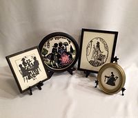 Four framed silhouette and needlepoint artworks shown together on stands against a white background.
